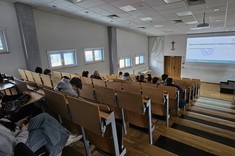 Dr hab. inż. Dominik Strzałka z Uczniami w Sali A61. Dr Strzałka prowadzi wykład o błędach matematycznych wykonywanych przez komputery. Widok z góry sali.