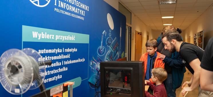 Hol budynku A. Stanowisko KN SKNI KOD. Na zdjęciu drukarka 3D i komputer. Student prezentuje grę.