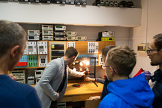 Laboratorium Energoelektroniki. Prowadzący pokazuje uczestnikom zasadę działania elektryki na przykładzie żarówek. Na zdjęciu prowadzący, stanowisko oraz uczestnicy.