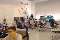 Mgr inż. Arkadiusz Stęchły z Uczniami w laboratorium Wirtualnej Rzeczywistości. Widok na salę oraz siedzących Uczniów. Pan Stęchły prezentuje projekty oraz omawia zajęcia realizowane w Sali VR.