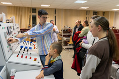 Laboratorium maszyn elektrycznych. Prowadzący tłumaczy i pokazuje działanie urządzeń. Na zdjęciu zwiedzający, konsola zarządzania oraz prowadzący.