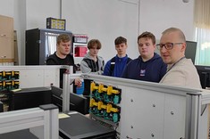 Mgr inż. Marcin Goral z Uczniami w Laboratorium automatyki, robotyki i sterowania. Pan Goral prezentuje Uczniom rozwiązania z zakresu automatyki przemysłowej. Widok na linię logistyczną